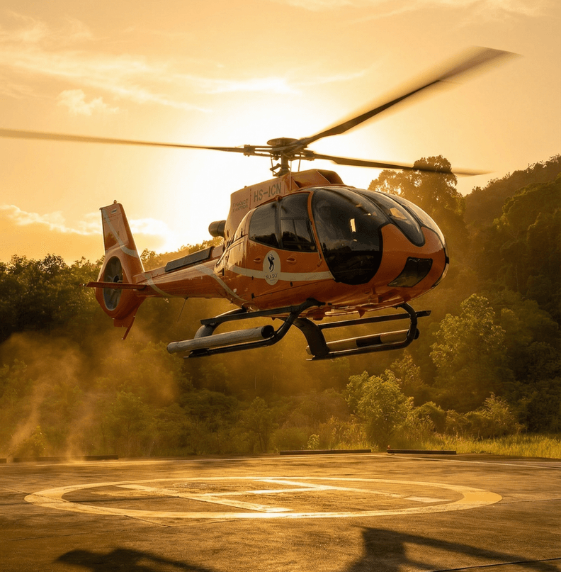 ภาพเฮลิคอปเตอร์ Airbus H130 สีส้มของ Silk Sky Air ขณะทะยานขึ้นจากรันเวย์ส่วนตัวในช่วงเวลาพระอาทิตย์ตกดิน ท่ามกลางบรรยากาศสีทองอร่ามและป่าเขตร้อนที่เขียวขจีของภูเก็ต สะท้อนถึงความหรูหราและความแม่นยำของการเดินทางทางอากาศระดับพรีเมียมในภาคใต้ของประเทศไทย