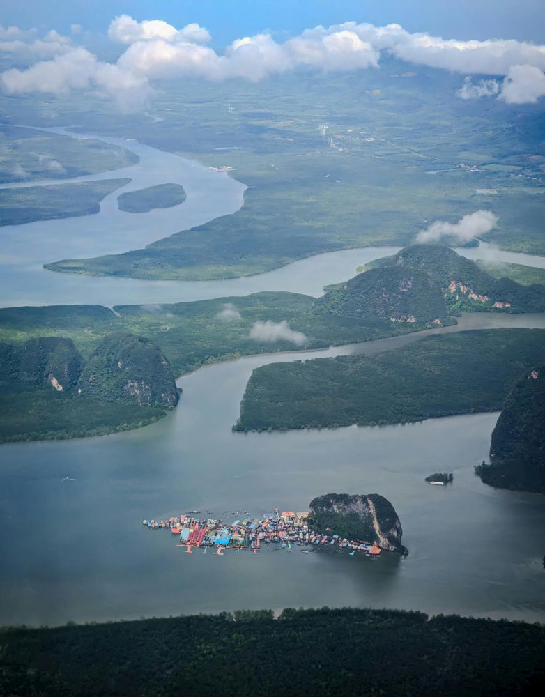 Aerial view from a Silk Sky Air helicopter over Phang Nga Bay showing Ko Panyee floating village with its colourful rooftops beside a limestone karst, surrounded by winding river channels and lush mangrove islands